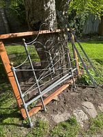Full view of iron headboard, footboard, side rails and wooden frame leaning against tree