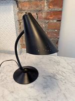 Side view of black metal desk lamp showing conical perforated shade and curved arm