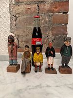 Group shot of five wood figurines with Coke bottle for scale