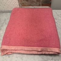 Folded pink wool blanket on marble surface, showing overall color and texture