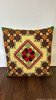 full view of square needlepoint pillow standing upright