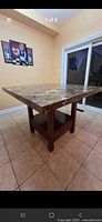 Full view of square faux-marble dining table showing base with drawer and shelf
