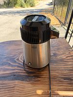Full view of the electric still showing stainless body, black top, and power cord