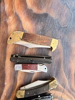 Four knives including brass/wood lockback, black ridged folder, small stainless/wood slipjoint, portion of another brass/wood knife