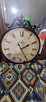 Front view of large round Paris wall clock with decorative scroll top