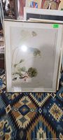 Full view of framed Asian duck and lotus print leaning on patterned rug