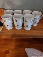 Full set of eight white porcelain cups with gold star pattern on wooden surface