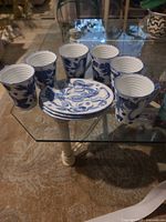 Six blue-and-white mugs and stacked plates on glass table