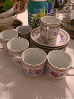 Group of demitasse cups and stacked saucers next to soda can for scale