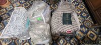 Four packaged bedding items on patterned rug: paisley comforter, grey plush comforter, plaid pillows, striped Ralph Lauren comforter