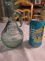 Front view of small glass olive oil jug beside soda can for scale