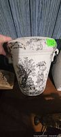 Overall view of white ceramic vase with black transfer design and metal handles