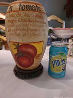 Vase front showing tomato artwork and text, alongside soda can for scale