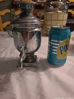 Full view of small metal samovar decanter beside soda can for scale