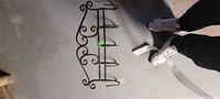 Top view of metal wall rack laying on floor showing scroll design and four hooks