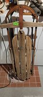 Full view of vintage wooden sled showing slatted deck, curved handle, steel runners and rope pull