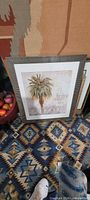 Full view of framed palm tree print placed on patterned rug