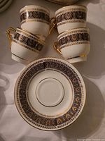 Four porcelain demitasse cups with ornate brown and gold band and one saucer