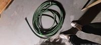 Coiled green garden hose with attached nozzle on floor