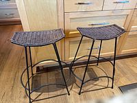 Two wicker-seat metal bar stools side by side