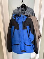 Three jackets hanging: blue/black front, gray, khaki behind