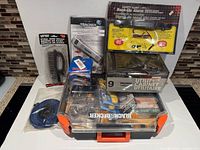 Overview of boxed utility cabinet, luggage scale, battery backup alarm, spark plugs, brush, rope and Black+Decker storage case