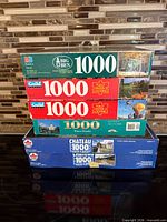 Stack of four 1000-piece puzzle boxes showing brands and partial images