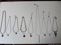 Nine silver-tone necklaces laid out showing pendants and chain styles