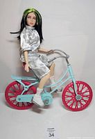 Billie Eilish doll seated on Barbie bicycle, side view