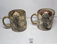 Front view of both mugs showing raised fish design and handles