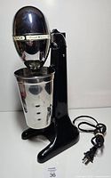 Front view of black Hamilton Beach DrinkMaster mixer with stainless cup and power cord visible