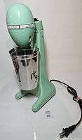 Front view of mint green Hamilton Beach DrinkMaster mixer with stainless cup and power cord visible