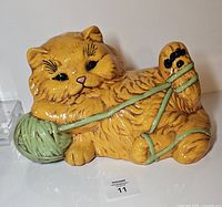 Front view of orange ceramic cat figurine with green yarn ball