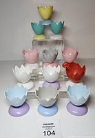 Group of 13 plastic cracked eggshell egg cups arranged on tiered stand, multiple colours visible