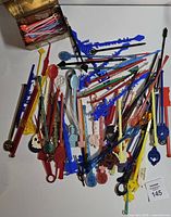 Pile of assorted colorful plastic swizzle sticks and picks spread on table with lot number card visible