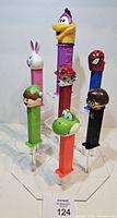 Front view of all seven character PEZ dispensers on clear stand