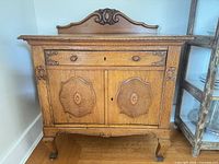 Front view of oak sideboard showing drawer, two carved doors, backsplash, cabriole legs