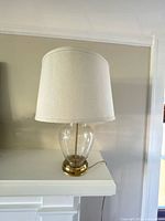 Full view of glass and brass table lamp with fabric shade on mantel