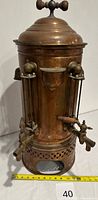 Full view of copper coffee urn with dual spouts and measuring tape for scale