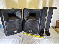 Front view of both EV Sx100+ speakers with two wall brackets and tape measure for scale
