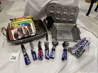 Group view of flatware bundles, loose utensils, roasting pan, grill basket, muffin pan, frying pan and cookbooks