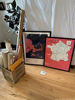 Box holding multiple rolled maps/posters; two framed maps beside it