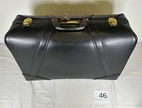 Closed black leather suitcase top view showing handle and gold-tone side latches