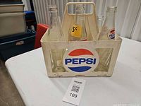 Front of white plastic Pepsi crate with six bottles, price sticker visible