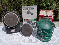 Three Coleman heaters with two boxes displayed on table