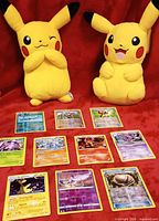 All ten holographic Pokémon cards laid out on red fabric, Pikachu plush in background not included