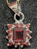 Front view showing square centre garnet, halo of round garnets, silver setting