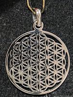 Front view of round openwork silver pendant showing flower of life pattern and bail