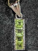 Front view of silver pendant showing peridot stones and etched border
