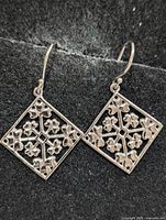 front view of both silver floral square earrings on black background